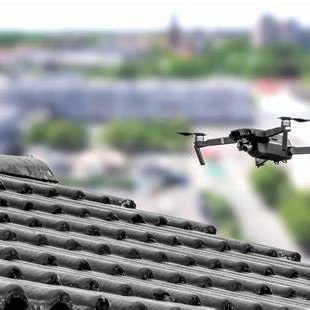 A drone flying above a rooftop with a blurred cityscape in the background.